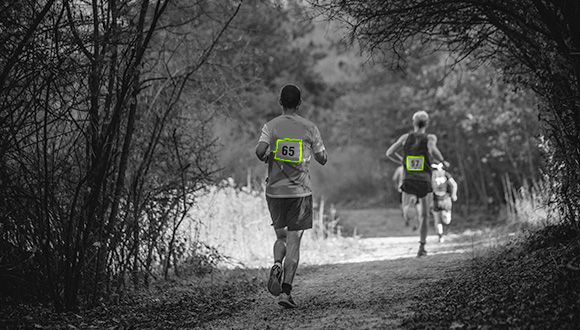 a number of runners with numbers on their backs running through a wooded area